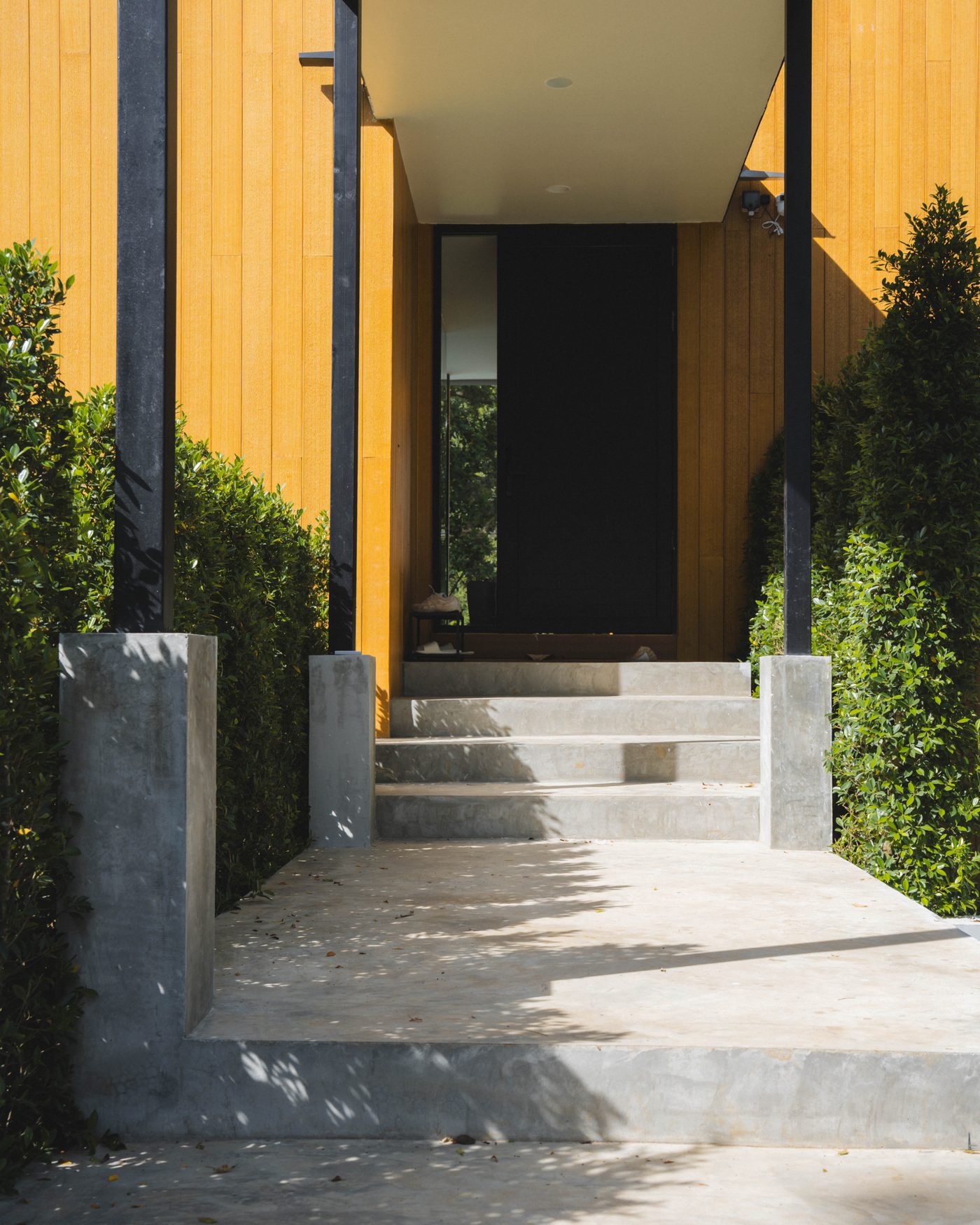 Finished entrance at Khao Yai: concrete steps between timber-clad walls and a clipped hedge