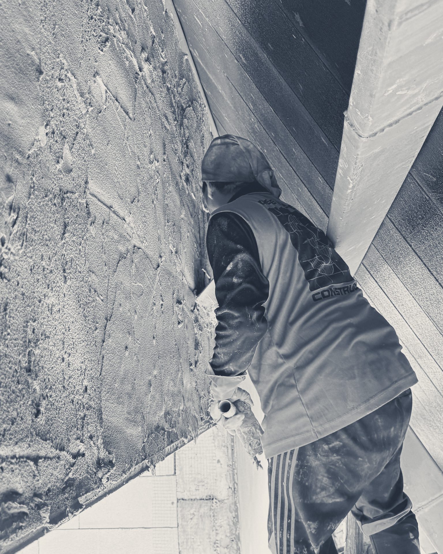 A plasterer, back to the camera, rendering a block wall under the roof edge