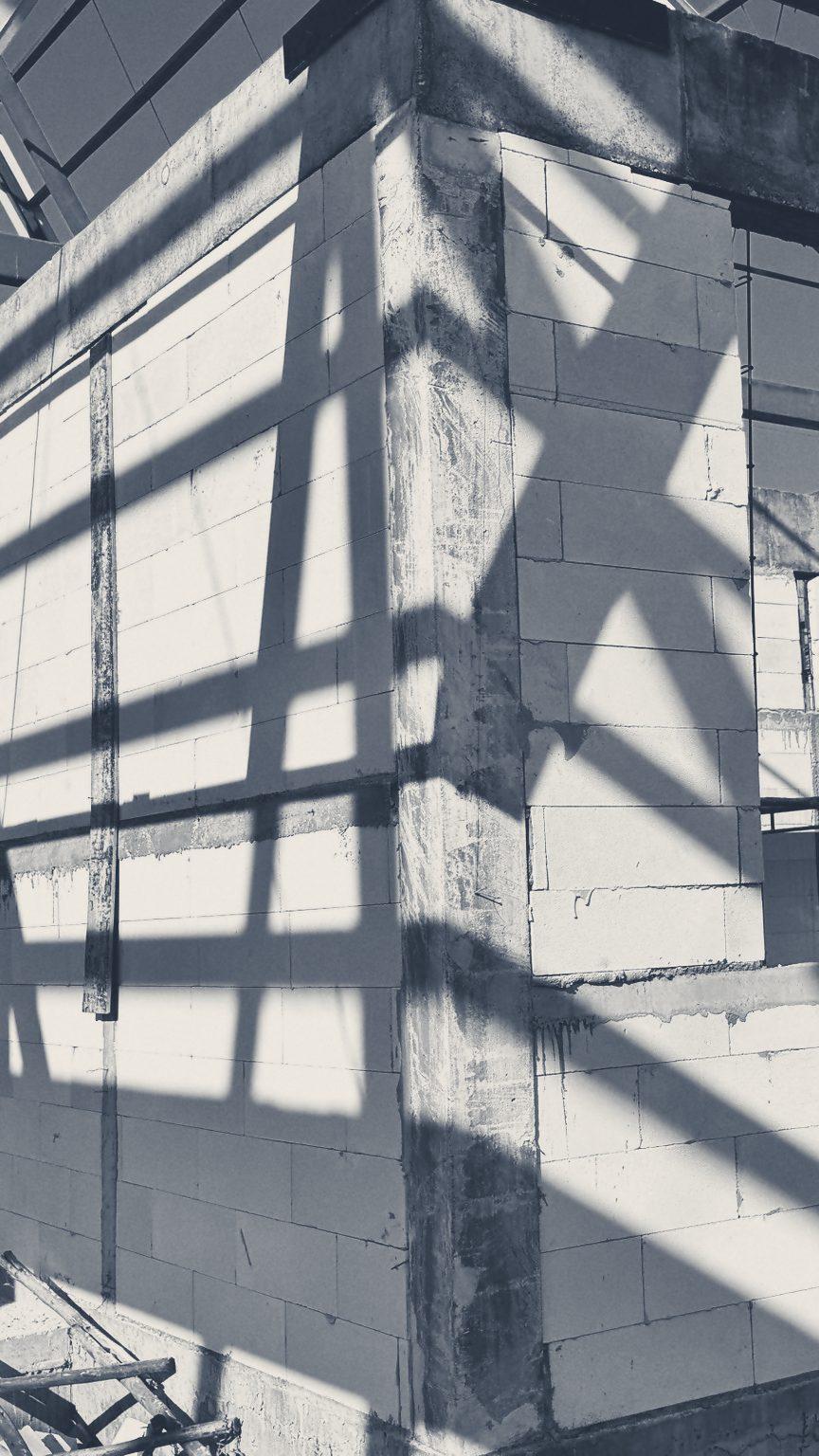 Block walls going up under the Club House steel roof frame, crossed by its shadows