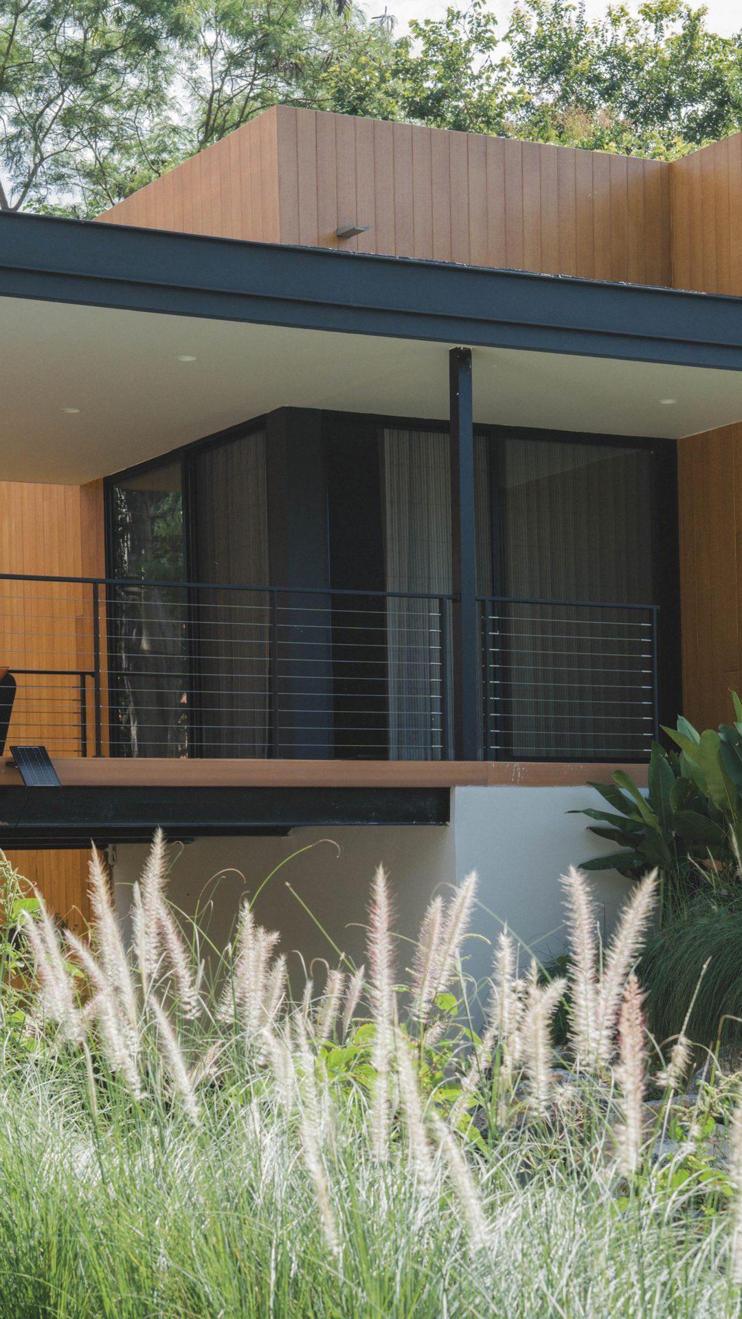 The finished Khao Yai villa: timber-clad walls and a covered terrace behind flowering grass