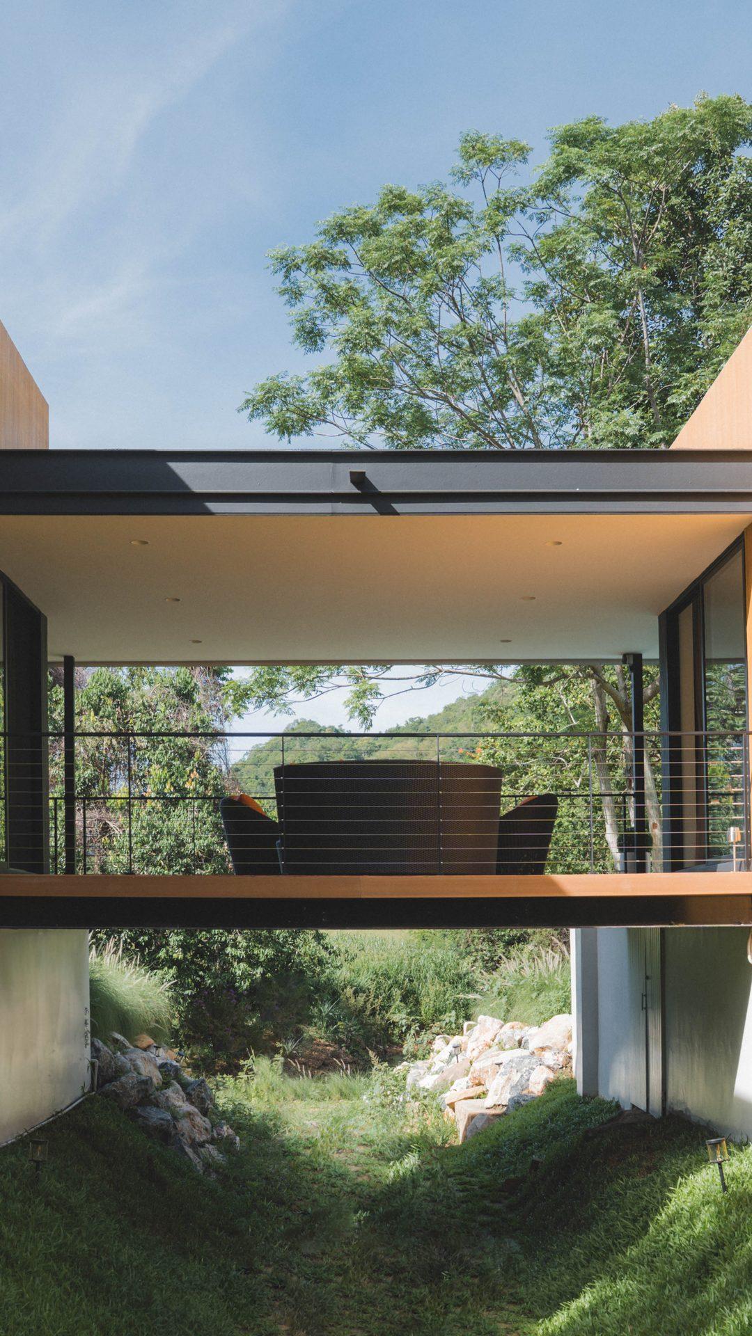 The Khao Yai villa in daylight: two timber-clad wings joined by a covered bridge over the garden