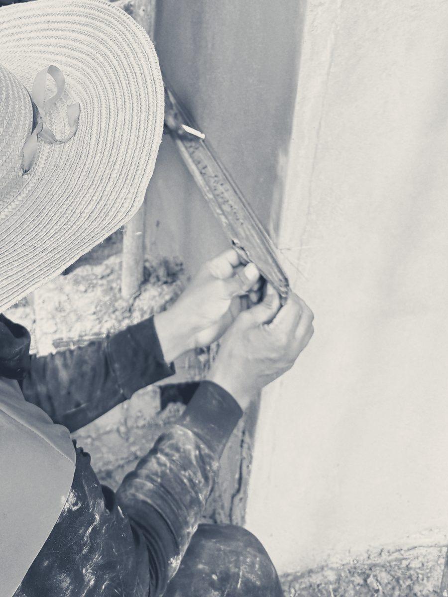 Hands holding a folding rule against fresh render, under the brim of a straw hat