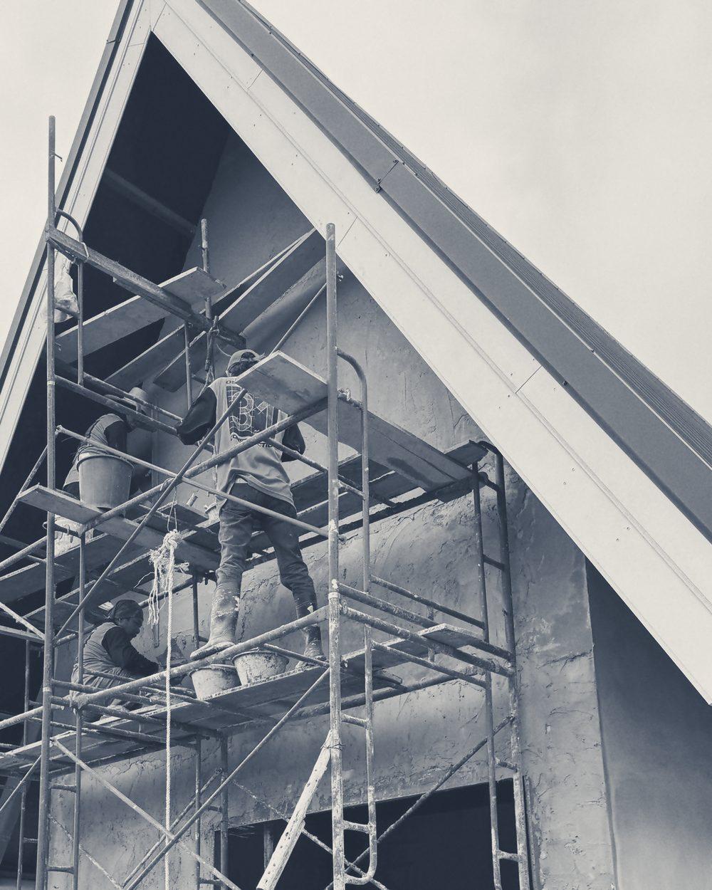 CON31 crew rendering a gable wall from the scaffold, backs to the camera.