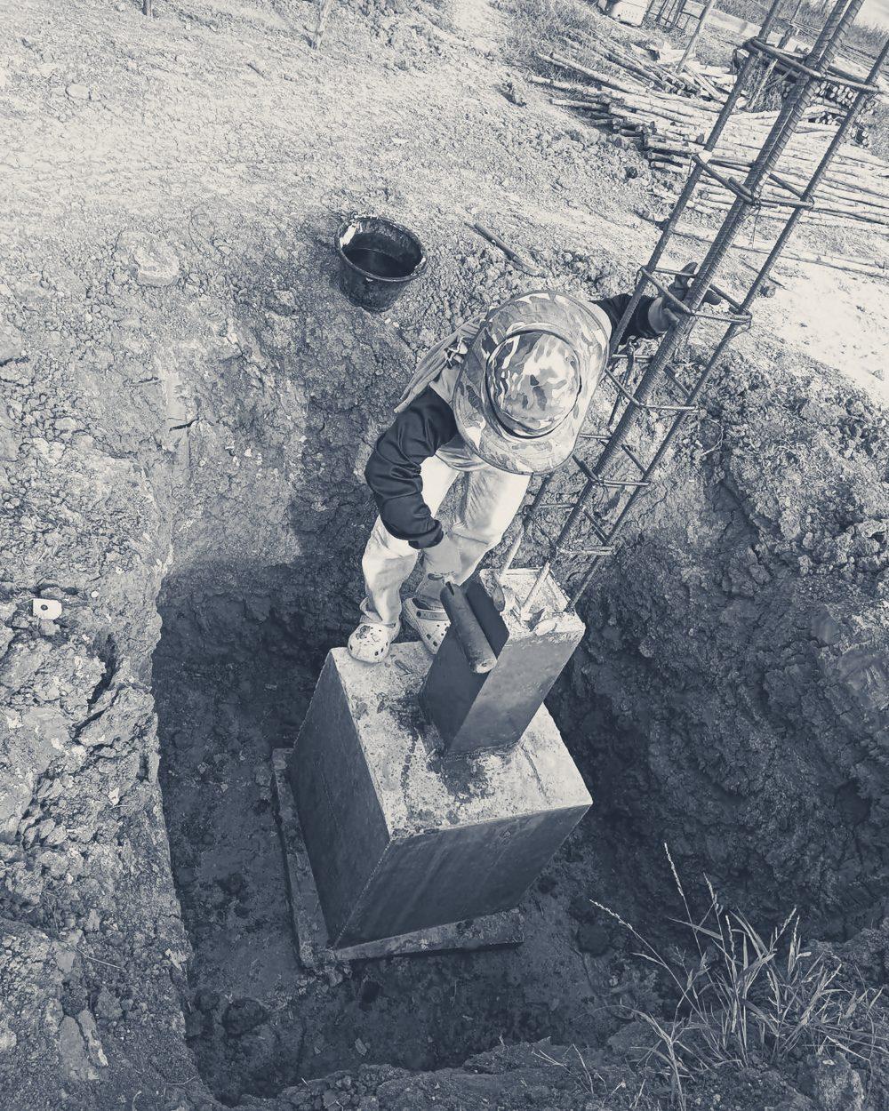 A tradesperson working on a column footing in its pit, seen from above.