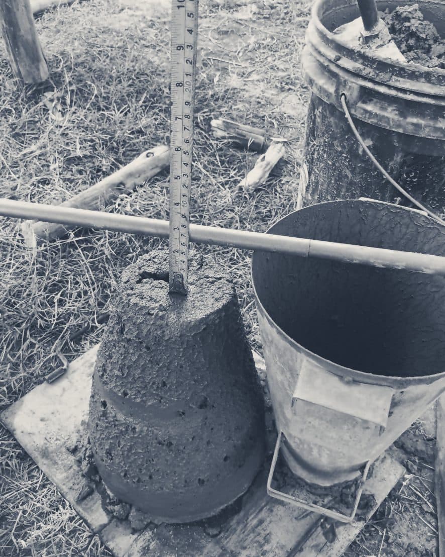 A concrete slump test: the slumped concrete next to its empty cone, with a tape measure