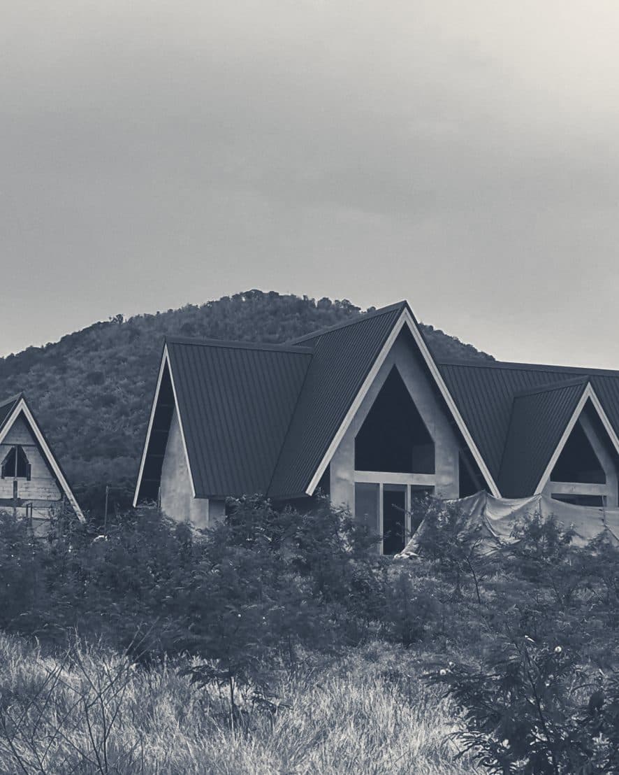 The Club House from the approach: three A-frames under construction in front of a wooded hill