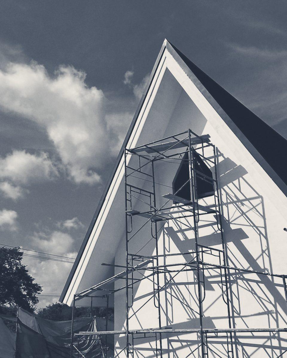 A white gable wrapped in scaffold, clouds behind