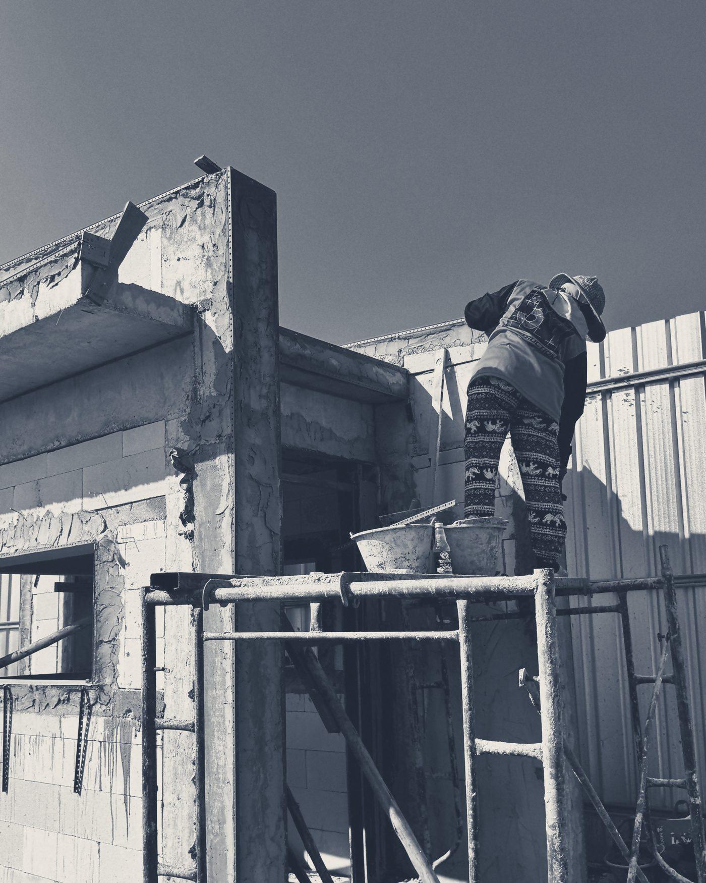 The guardhouse walls going up, a worker on the scaffold with his back to the camera