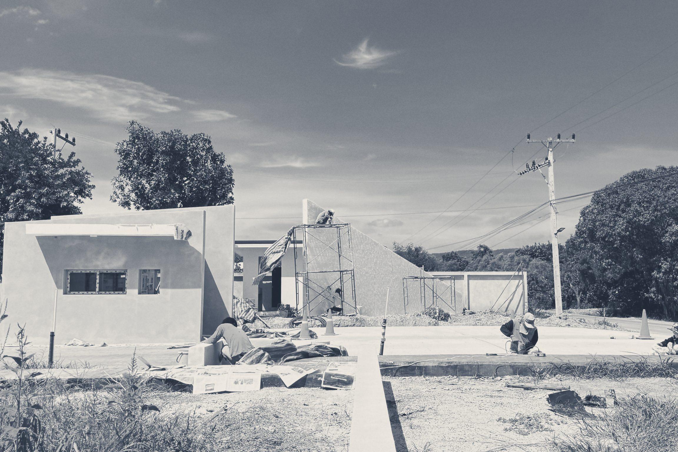 The guardhouse and the slanted feature wall near completion. Scaffold still stands on the wall while a crew works on the paving in front.