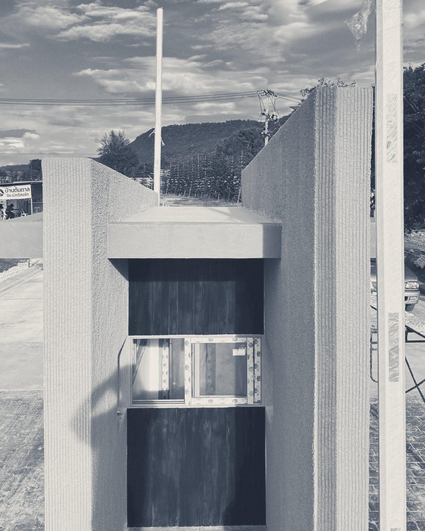 The Main Gate guardhouse up close: a dark timber panel and window between two walls of textured render