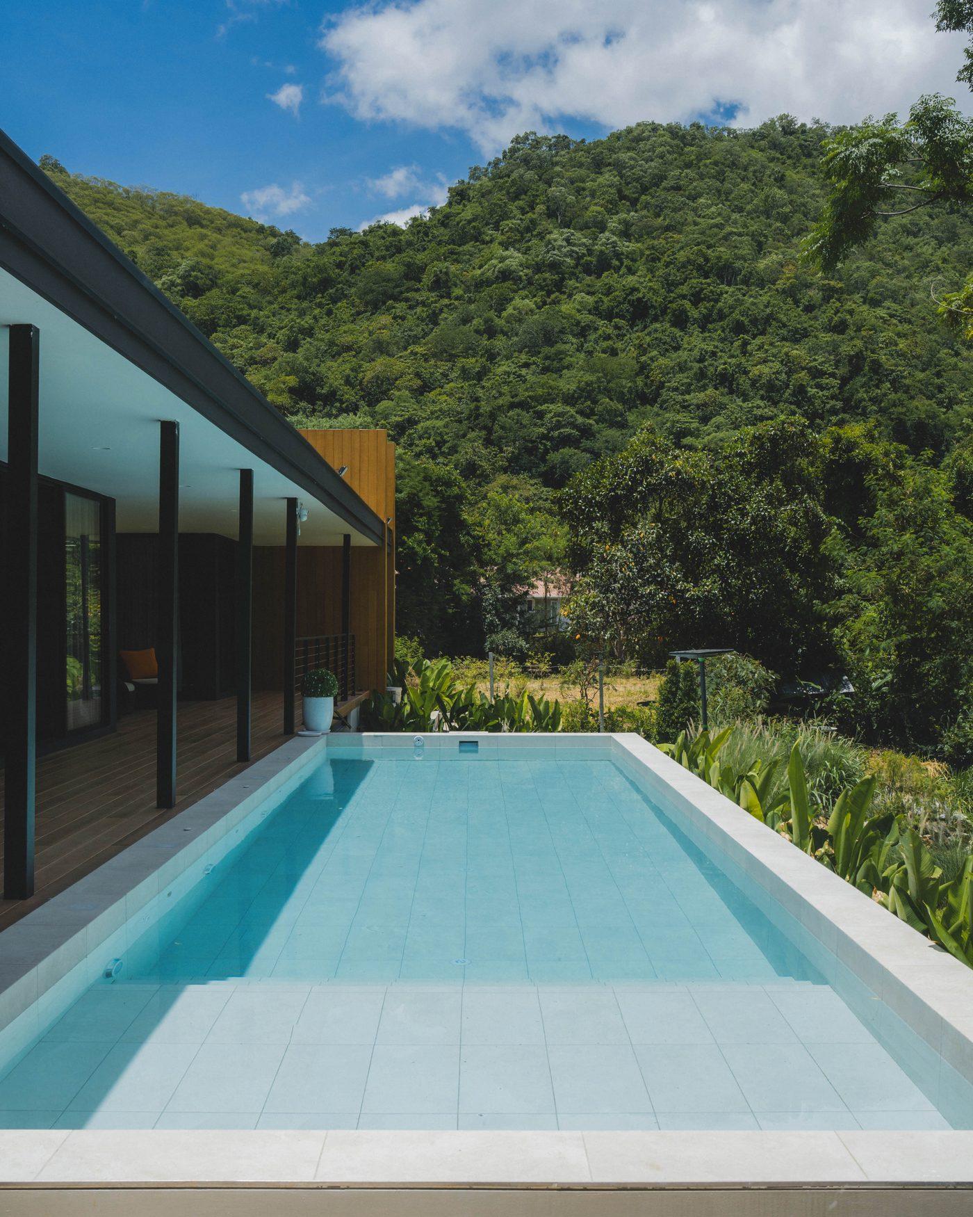 The pool running along the glazed living wing, with wooded hills behind