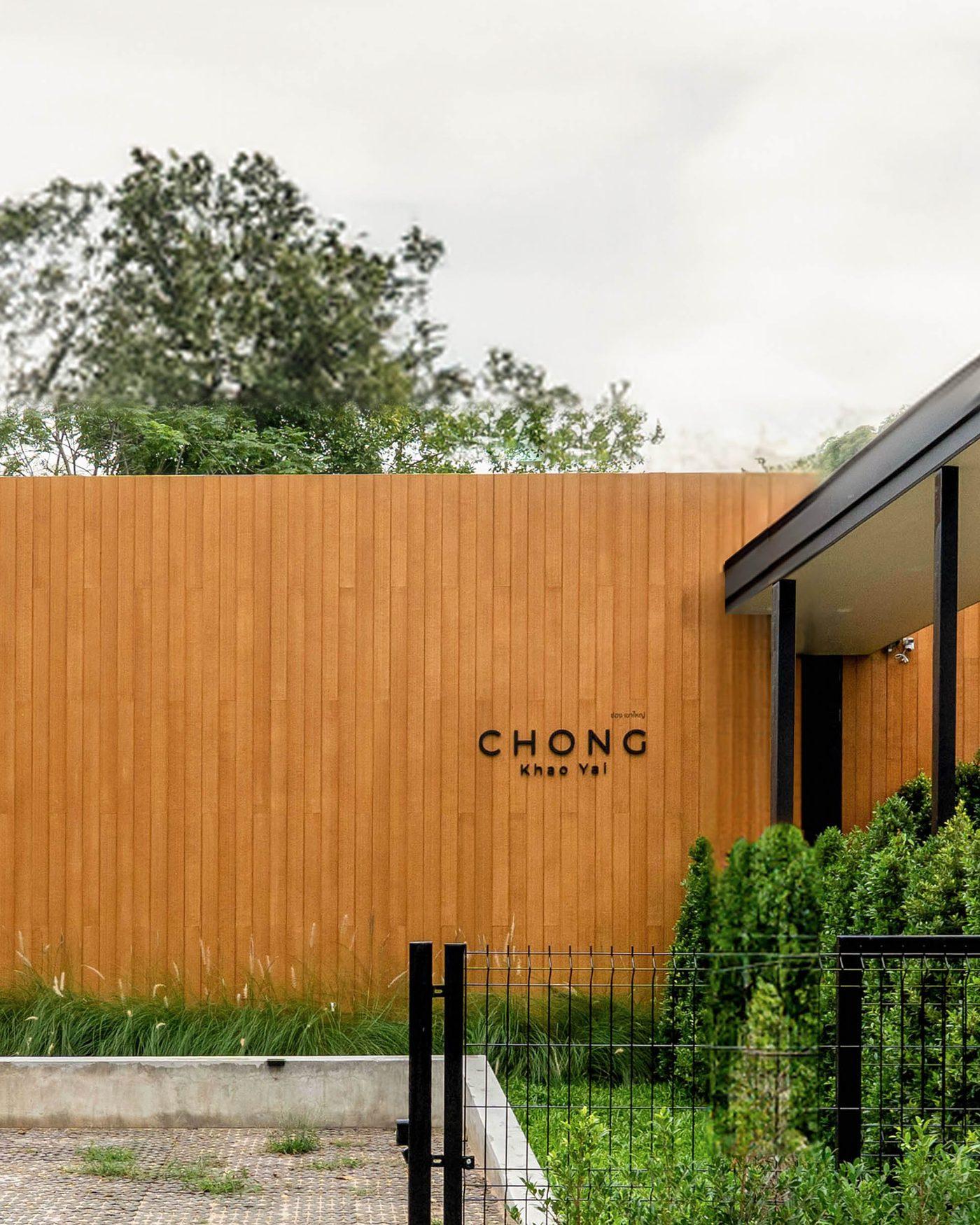 The finished timber wall carrying the house name, with a corner of the entrance canopy at the right and the gate in front