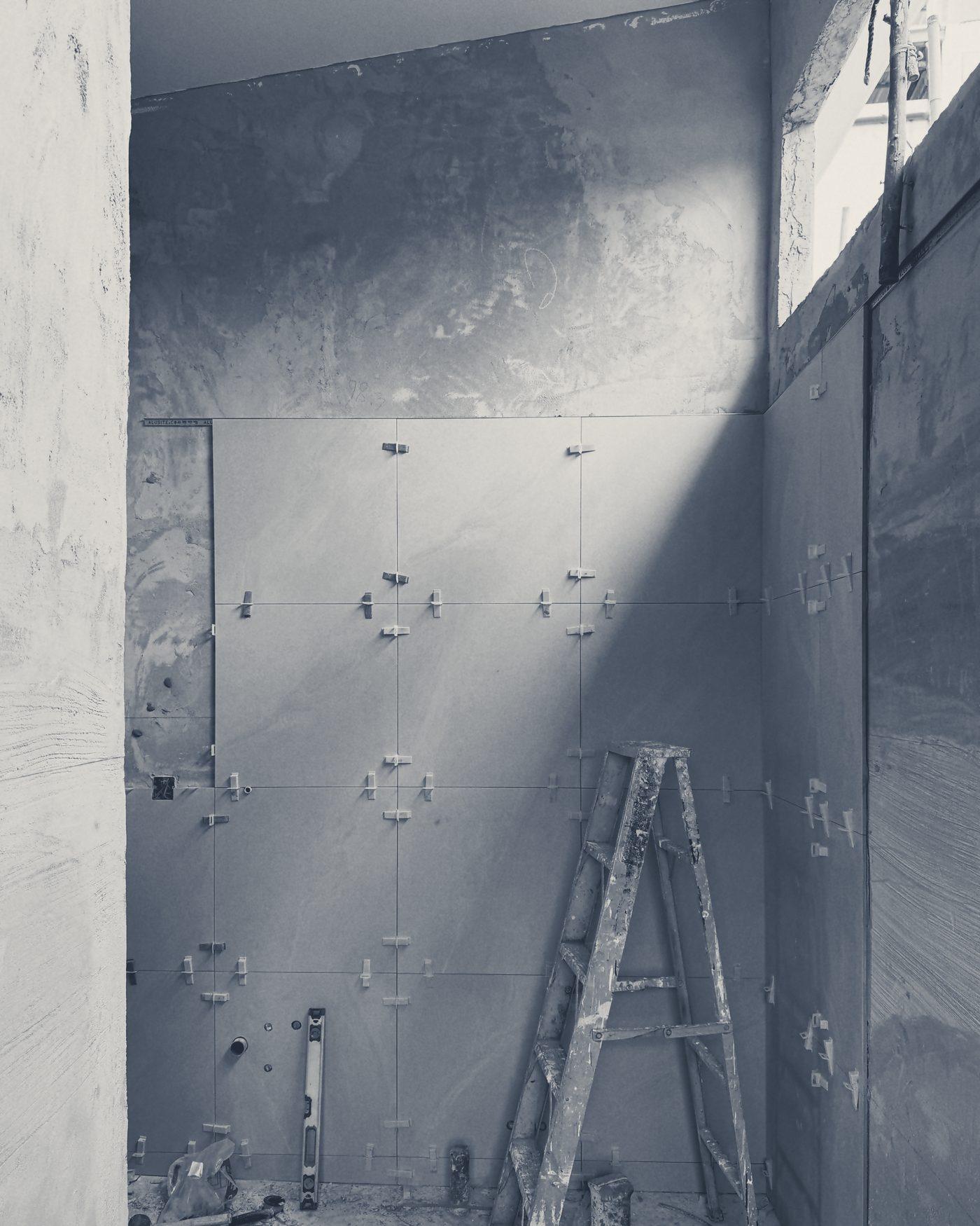 Wall tiles set out with levelling clips, a ladder in the corner