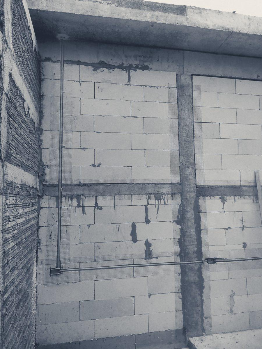Lightweight concrete block walls before rendering, with mesh over the joints and conduit fixed to the blocks. A brick wall is at the left.