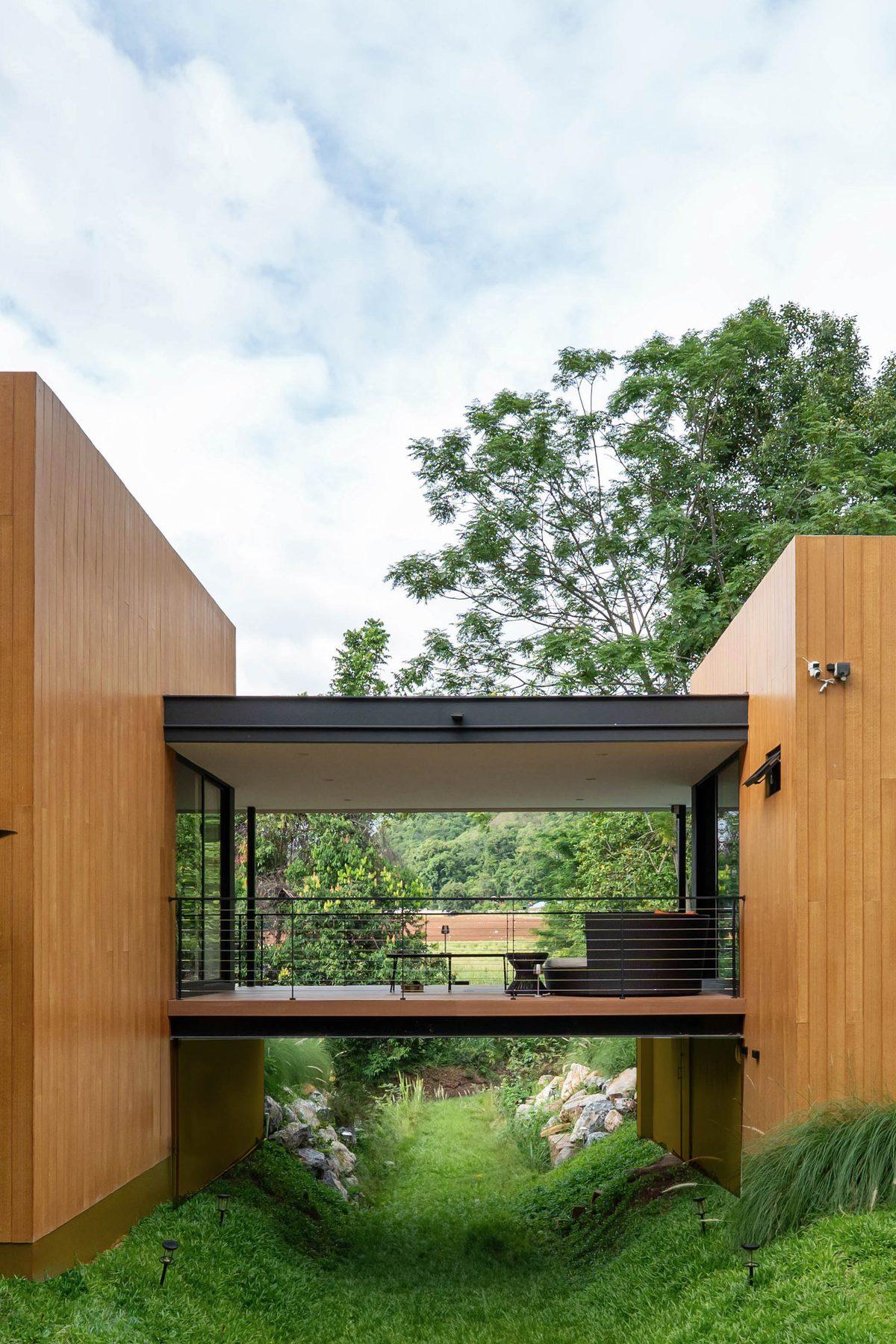 Covered bridge joining the two timber-clad wings of the Khao Yai villa, above a grassy gully