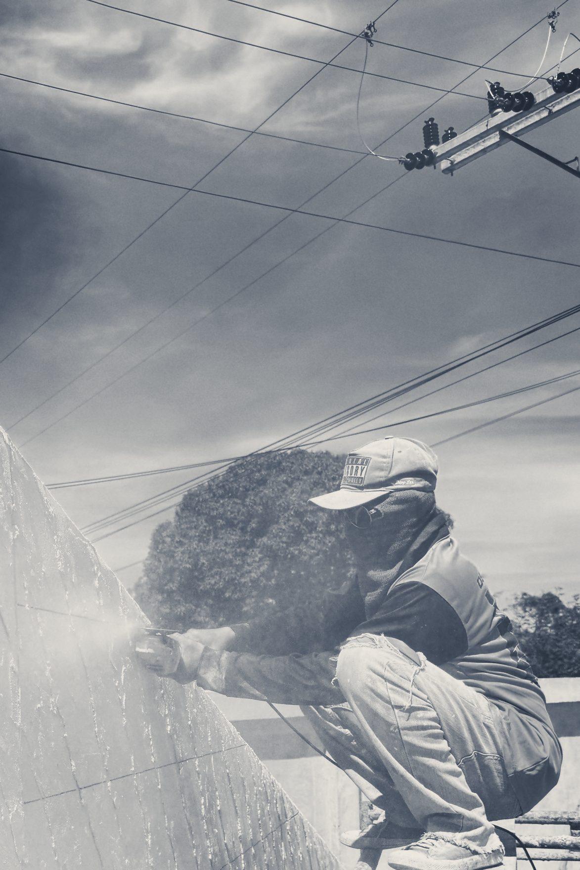 Worker on a plank platform finishing the surface of a tall rendered wall