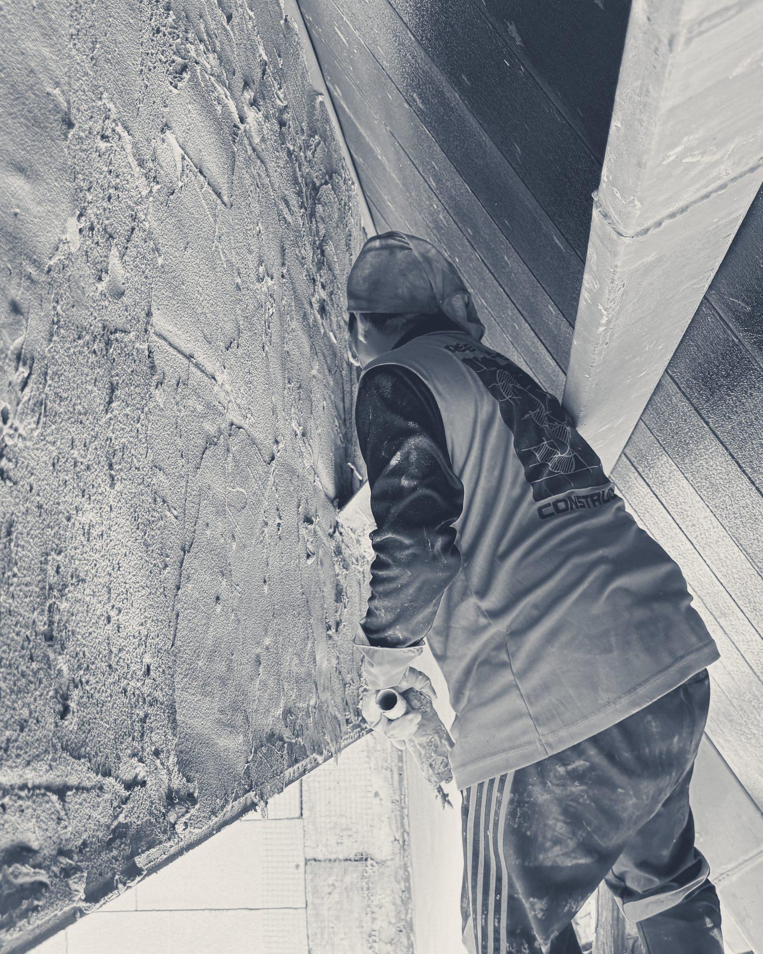 A plasterer, back to the camera, rendering a block wall under the roof edge